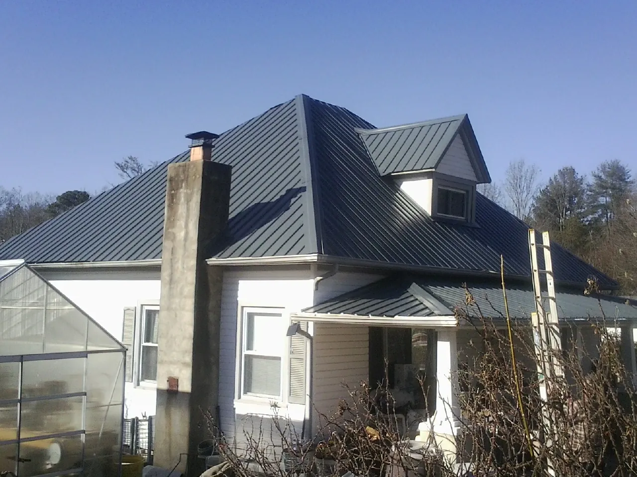 Dark blue standing seam metal roof on a white farmhouse with dormer — Slate & Tile Roof Repair by Roofing Brothers in North Collins