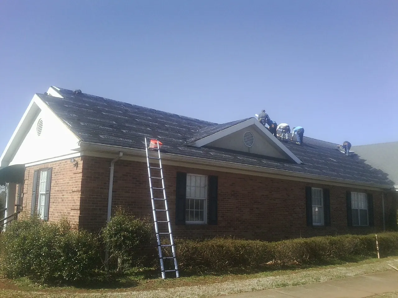 Crew tearing shingles off a brick ranch roof with a ladder set — Metal Roof Repair work by our crew in North Collins