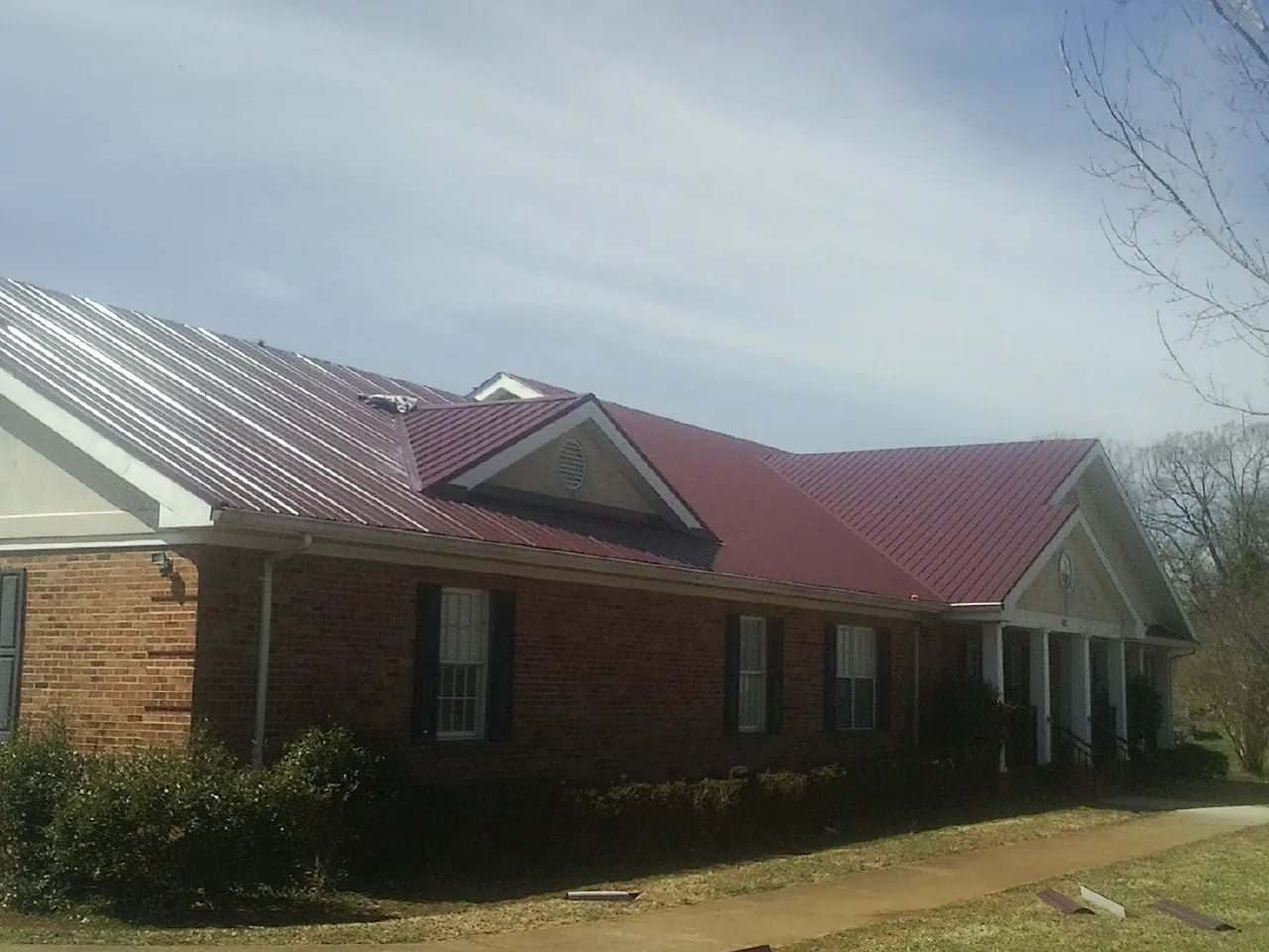 Red metal roof with gabled entries on a long brick building, from a Hail Damage Roof Repair job in North Collins