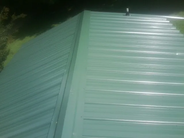 New green metal panels meeting at the ridge of a roof — Flat Roof Repair work by our crew in North Collins