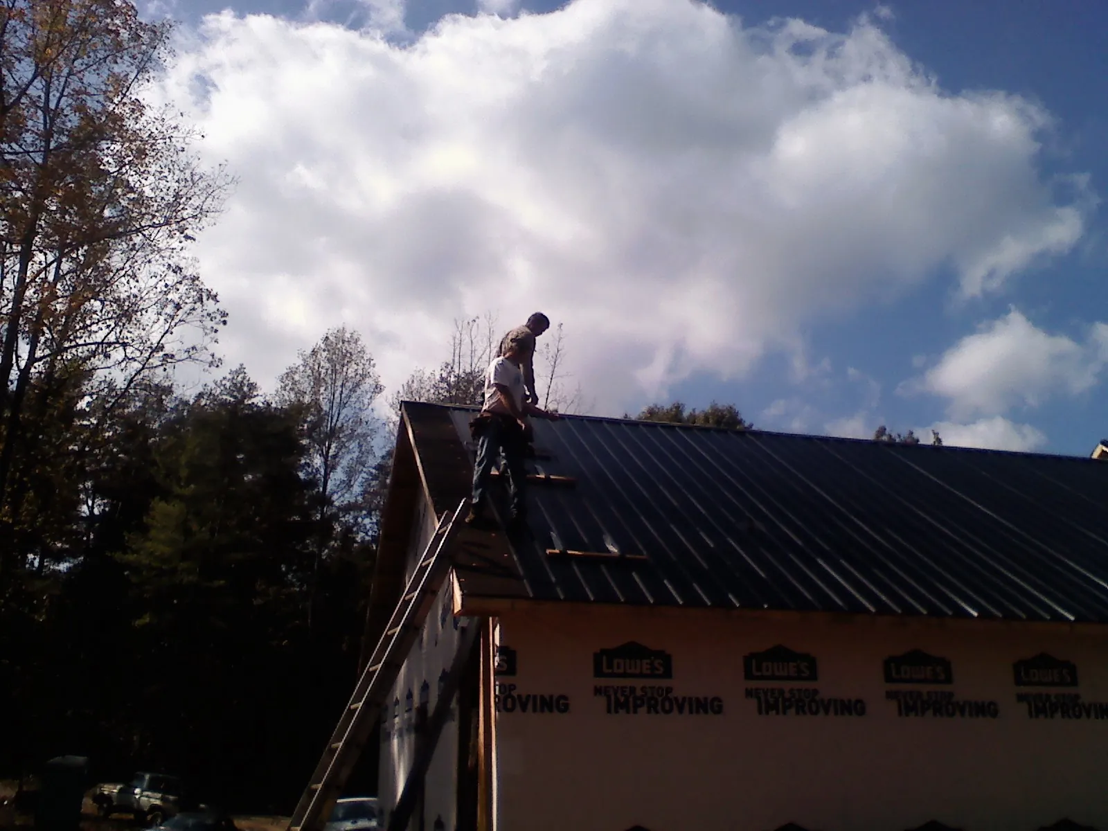 Roofer fastening dark metal panels high against a cloudy sky, from a Roof Inspection job in North Collins