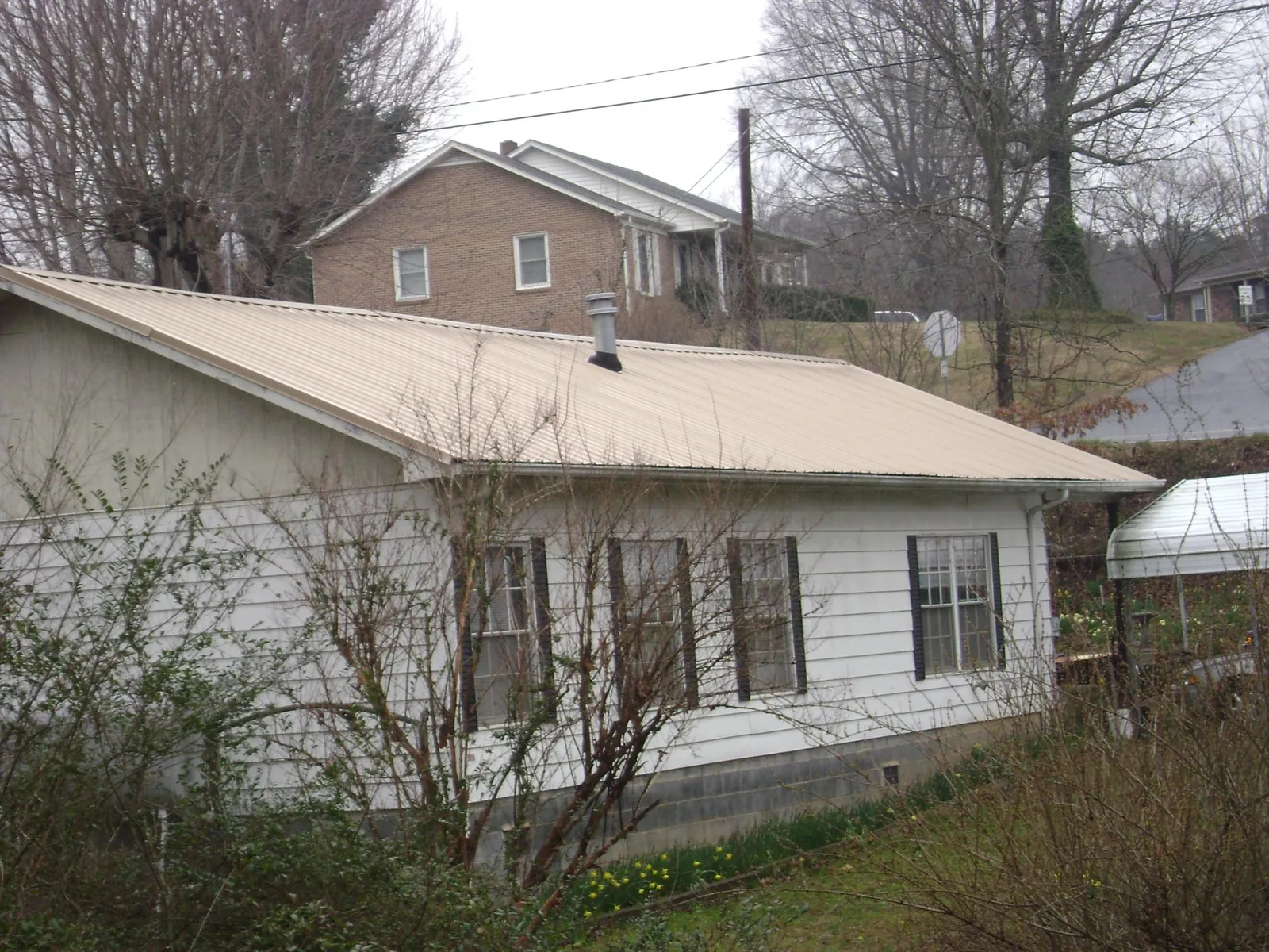 Tan metal roof on a white sided house set into a hillside — Commercial Roofing by Roofing Brothers in North Collins