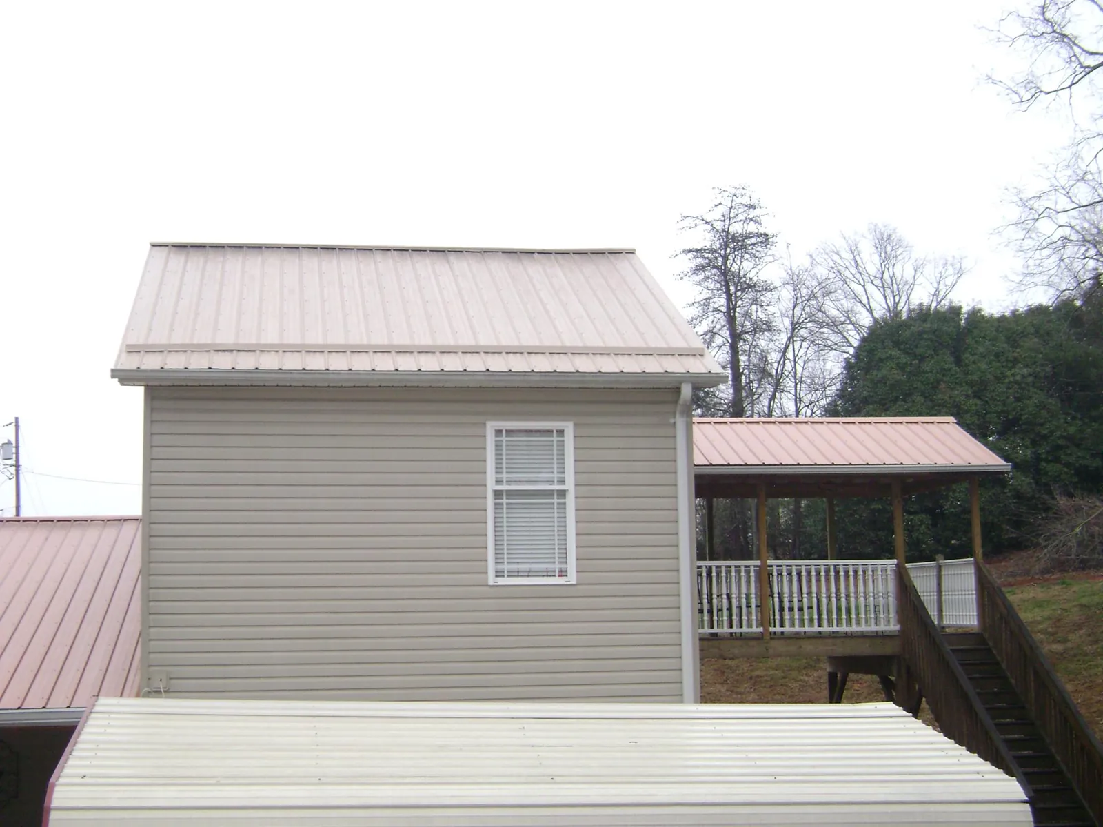 Tan metal roofs on a two story addition and attached porch, from a Roof Replacement job in North Collins